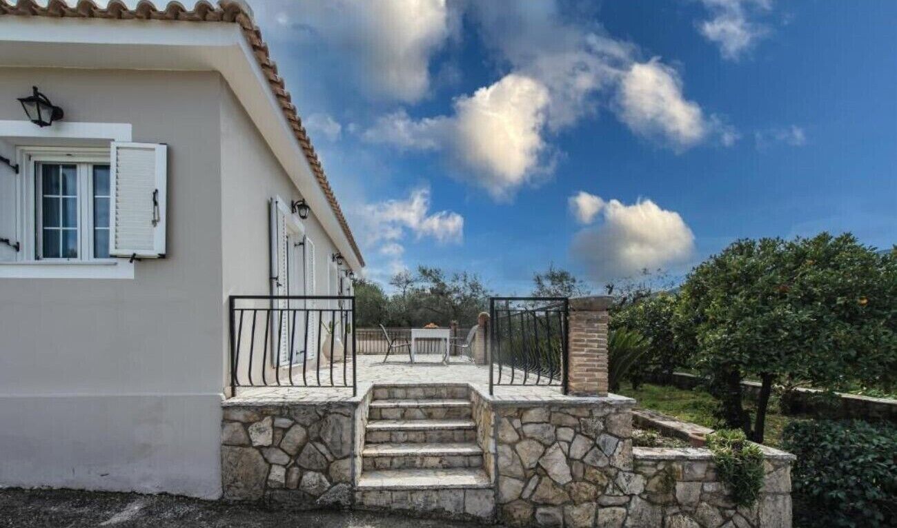 Une maison avec un escalier en pierre menant à un patio, une façade blanche et un ciel d’un bleu limpide.