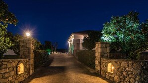 Ein gepflasterter Weg führt zu einem Gebäude mit Ziegeldach, umgeben von Grünflächen und Steinmauern.