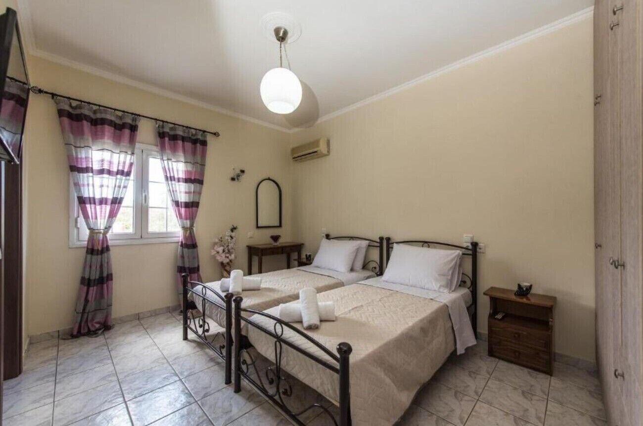 A bedroom with two beds, a bedside table, a nightstand, a window with curtains, and a ceiling light.
