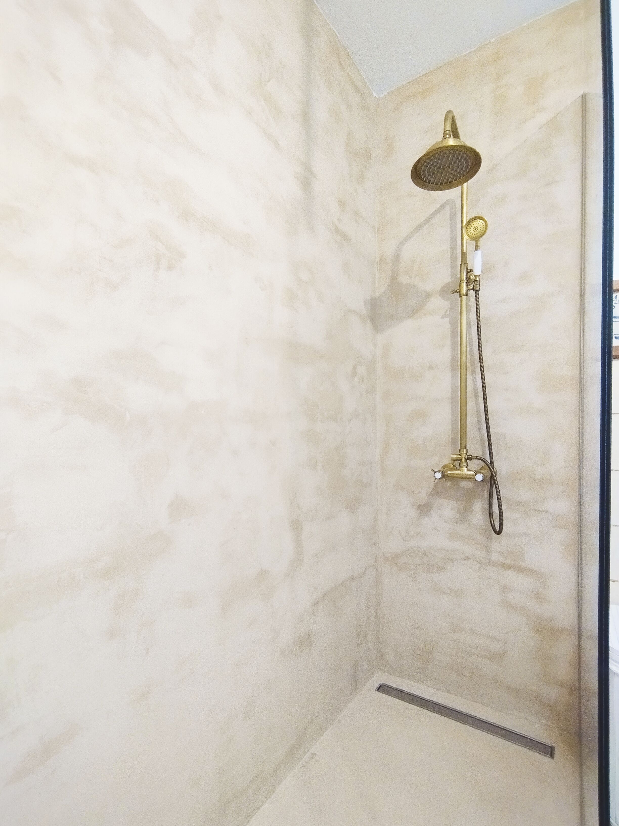 Un baño con pared de mármol, cabezal de ducha dorado y ducha de mano.