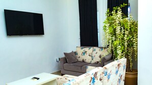 A living room with a flat-screen TV mounted on the wall, a sofa with floral upholstery, a coffee table, and a potted plant. - The Point Hotel and Suites (Jos)