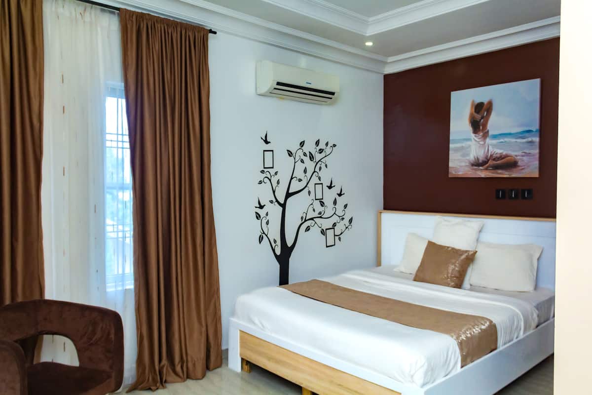 A bedroom with a bed, brown curtains, a wall-mounted air conditioner, a painting, and a tree decal.