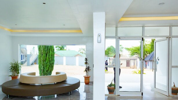 A modern lobby with a circular seating area, a glass door entrance, and potted plants. - The Point Hotel and Suites (Jos)