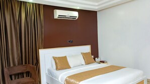 A hotel room with a bed, a chair, an air conditioning unit, and a curtain. - The Point Hotel and Suites (Jos)