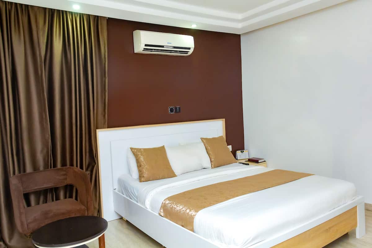 A hotel room with a bed, a chair, an air conditioning unit, and a curtain.