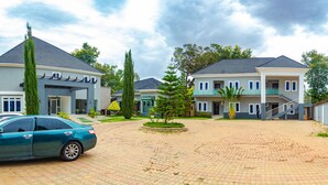 A modern hotel with a paved courtyard, a car parked in front, and a Heineken sign. - The Point Hotel and Suites (Jos)