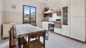 A kitchen with a dining table, chairs, a clock, cabinets, and a window. - Holiday Home "Casa Degli Zii Appartamento Guido" with Shared Terrace, Balcony & Wi-Fi (Luni)