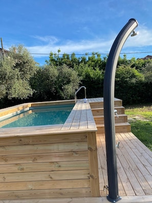 A wooden deck with a hot tub, metal railings, and a clear blue sky.