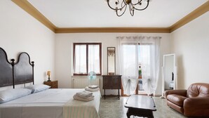 A bedroom with a bed, a wooden nightstand, a table, a leather armchair, and a view of the outside. - Holiday Home "Casa Degli Zii Appartamento Guido" with Shared Terrace, Balcony & Wi-Fi (Luni)