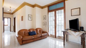 A living room with a brown leather sofa, a television on a wooden table, and a door leading to another room. - Holiday Home "Casa Degli Zii Appartamento Guido" with Shared Terrace, Balcony & Wi-Fi (Luni)