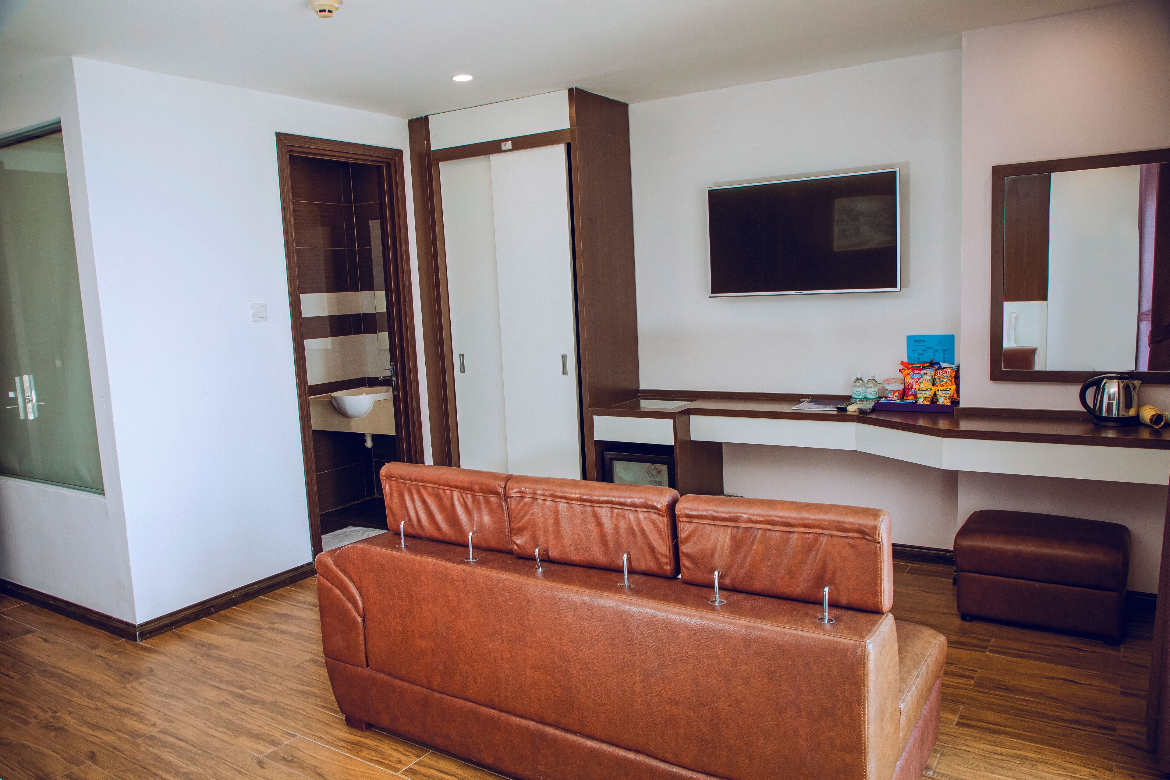 Een moderne hotelkamer met een leren bank, een bureau met een flatscreen televisie, een spiegel en een garderobe.