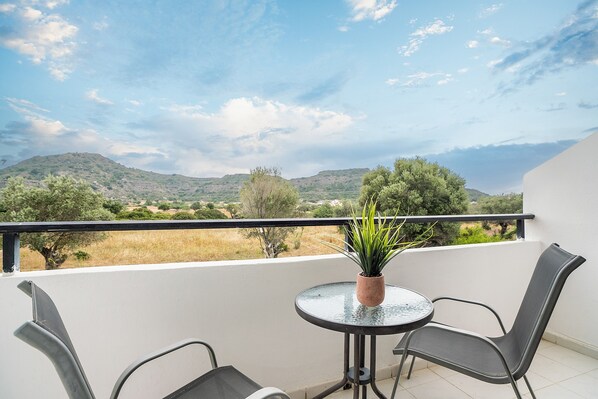 A balcony with a table and chairs, a potted plant, and a view of distant hills and trees.