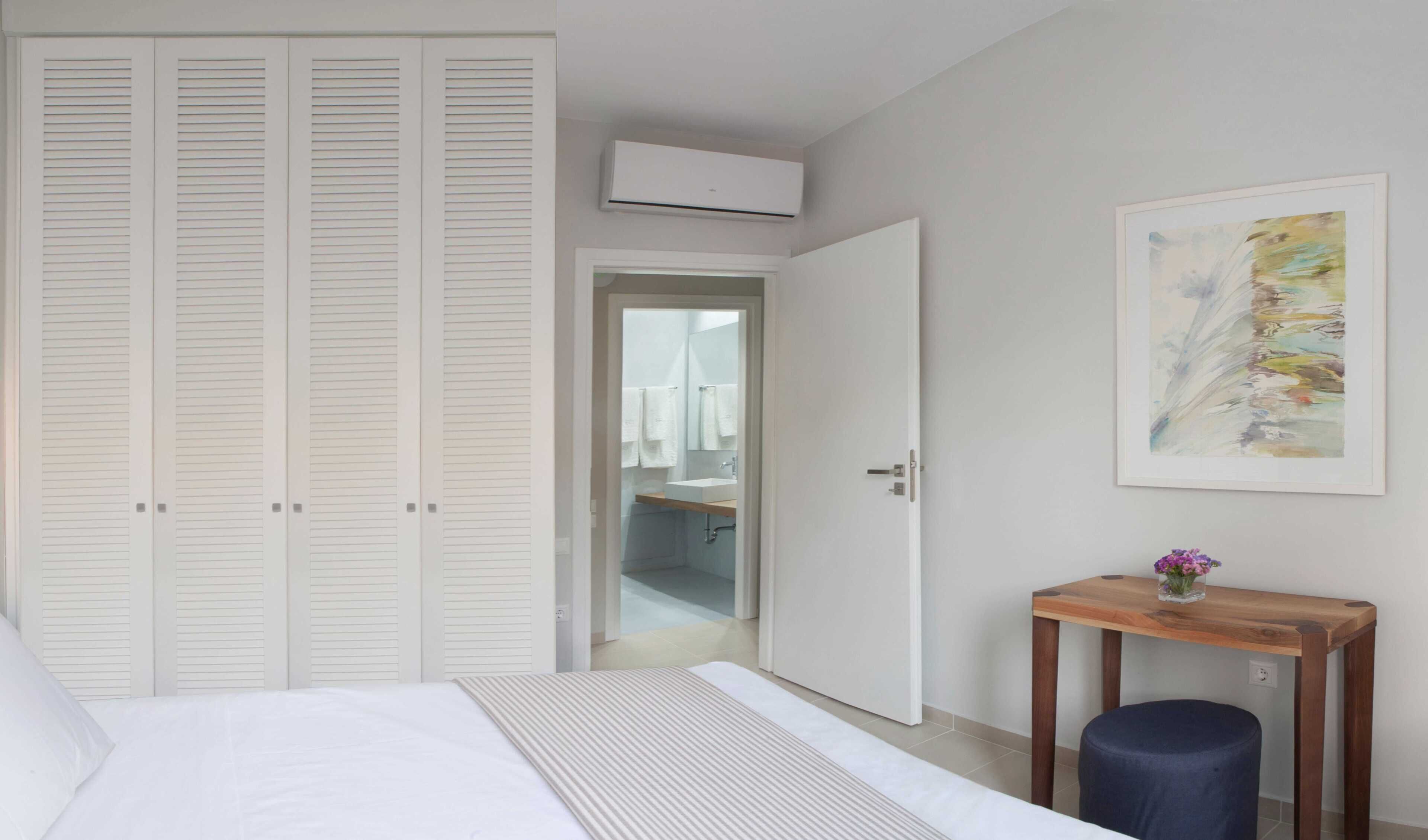 Een slaapkamer met een bed, een houten nachtkastje, een witte kledingkast en een badkamer die door een open deur zichtbaar is.