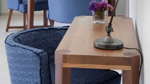 Una habitación con un escritorio de madera, una silla azul, un sofá azul, una lámpara de escritorio y una ventana con vistas a árboles.