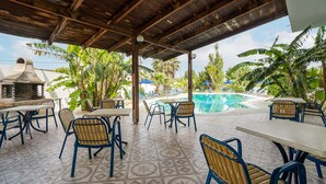 An outdoor patio with tables and chairs, a pool, and tropical plants.