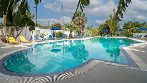 A swimming pool with lounge chairs and umbrellas, surrounded by palm trees and a clear sky.