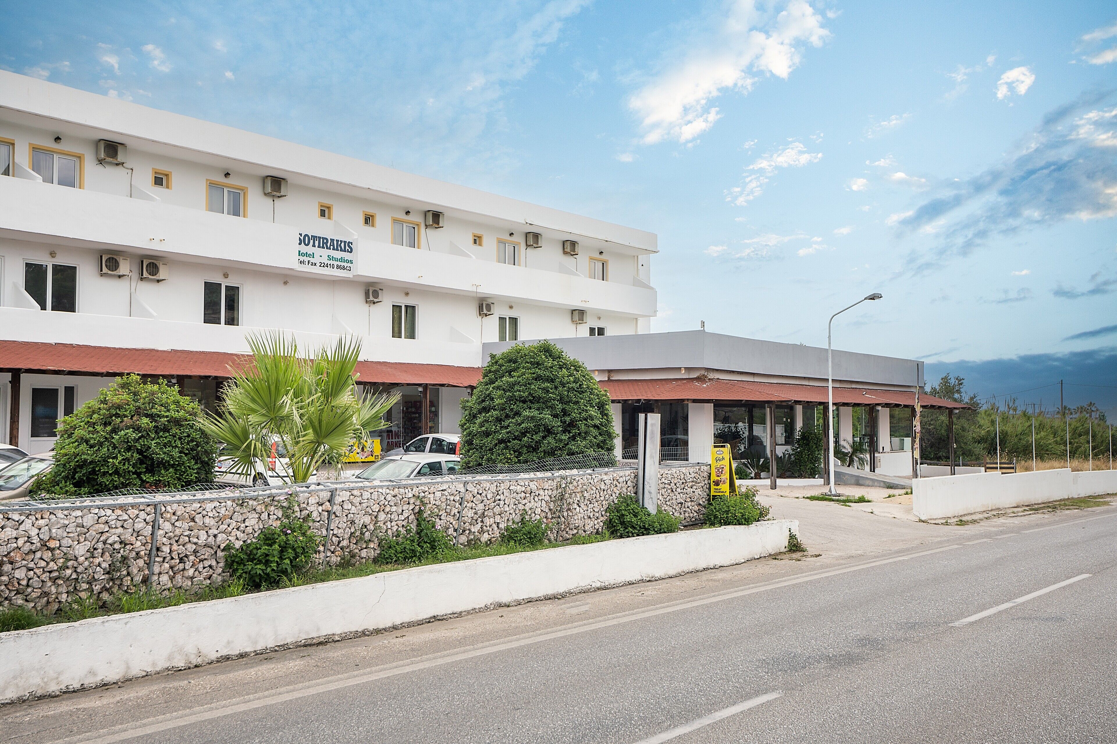 A hotel with a white facade, multiple windows, and a stone wall with greenery.