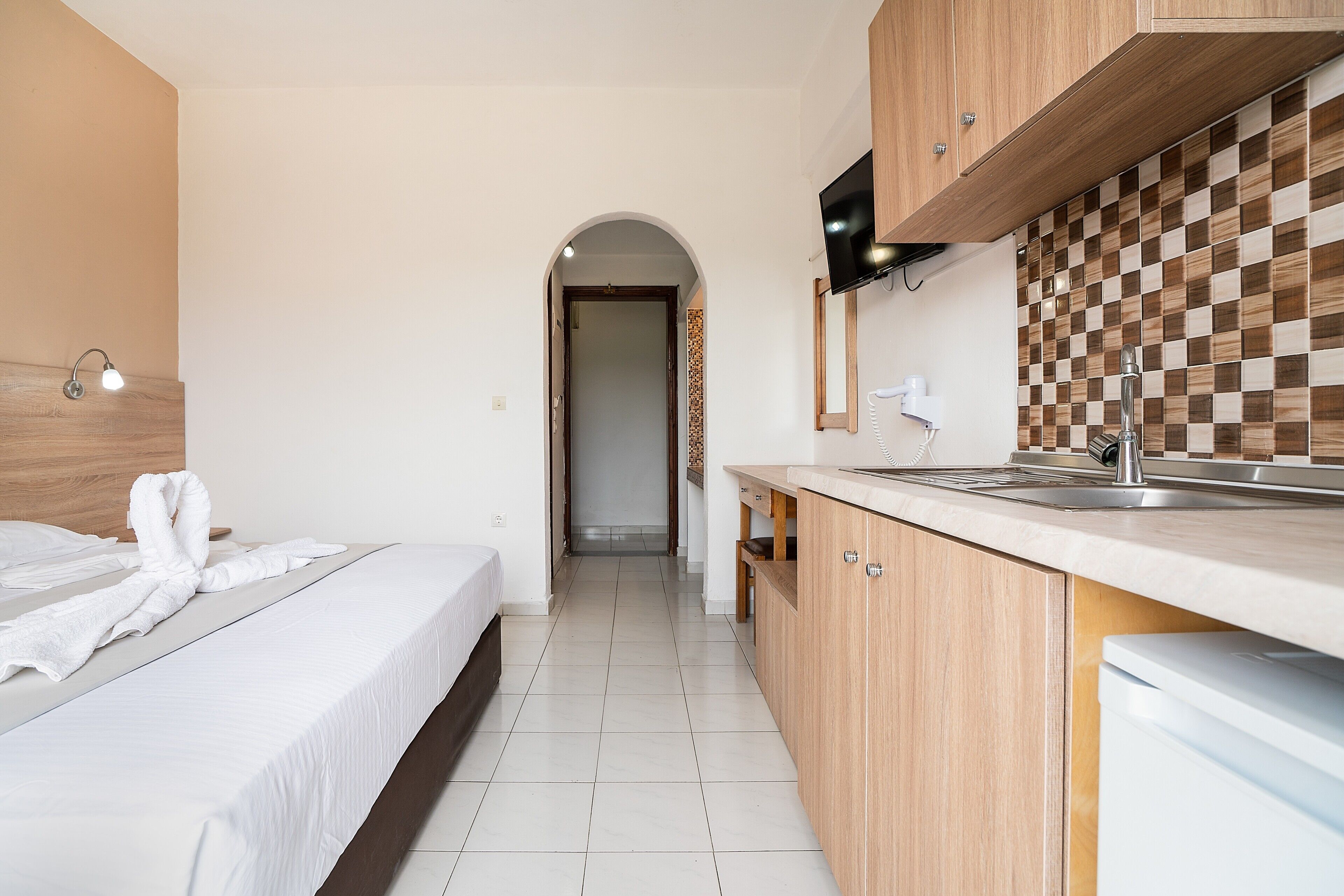 A hotel room with a bed, a kitchenette, a TV, and a tiled floor.