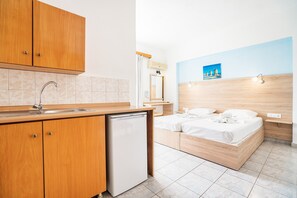 Quarto de hotel compacto com cozinha compacta, cama com roupa de cama branca, cabeceira de madeira e pequena mesa de cabeceira.