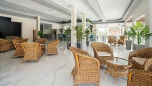 Een ruime lobby met rieten meubels, een glazen bijzettafeltje en een modern plafondontwerp.