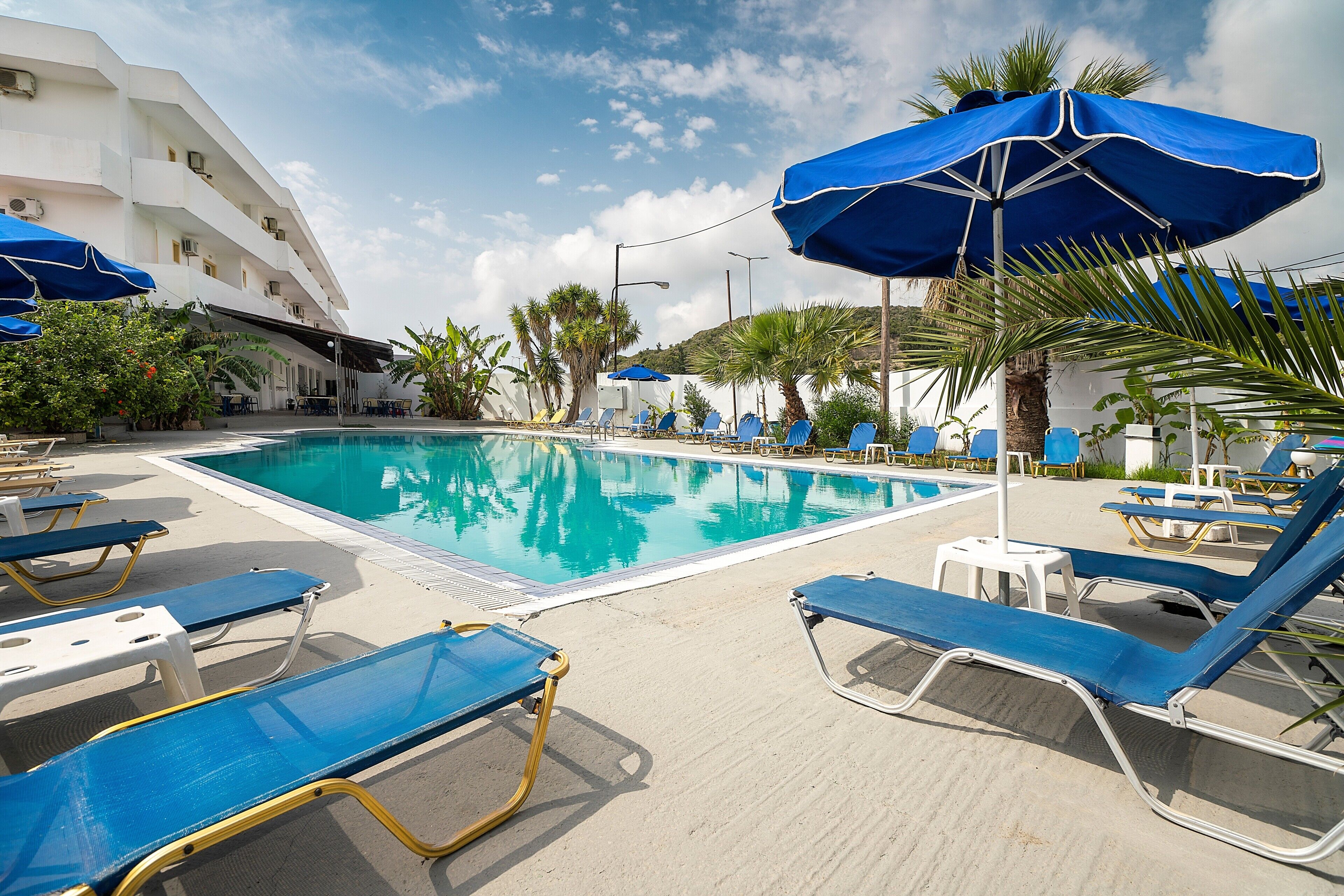 A poolside area with lounge chairs and umbrellas, a clear pool, and a building with balconies.
