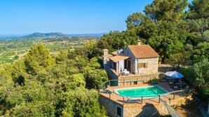 A stone house with a swimming pool, surrounded by trees and a view of the countryside.