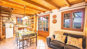 A cozy kitchen with wooden beams, a dining table, and a leather sofa with floral cushions.