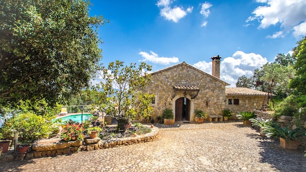 A stone building with a tiled roof, a cobblestone courtyard, and potted plants.