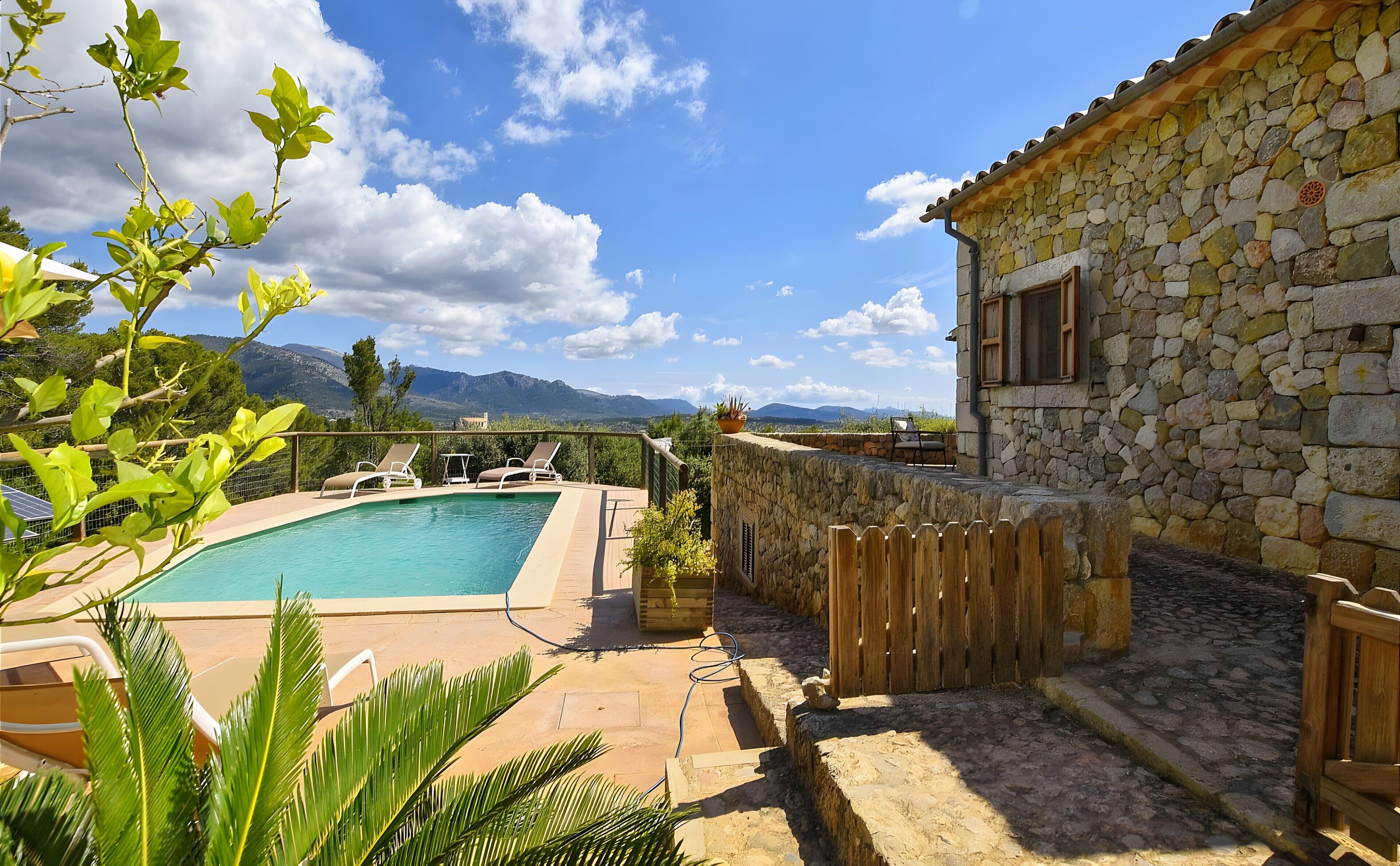 A pool with lounge chairs, a stone building, and a view of mountains.