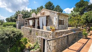 A stone house with a balcony, surrounded by greenery.