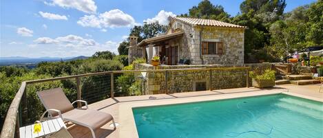 A stone villa with a swimming pool, outdoor seating, and a view of the landscape.