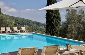 Piscina com água azul cristalina, rodeada por espreguiçadeiras e uma mesa com garrafa e copo.