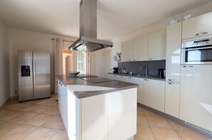 Uma cozinha moderna com ilha central, eletrodomésticos de aço inoxidável e armários em tons claros.