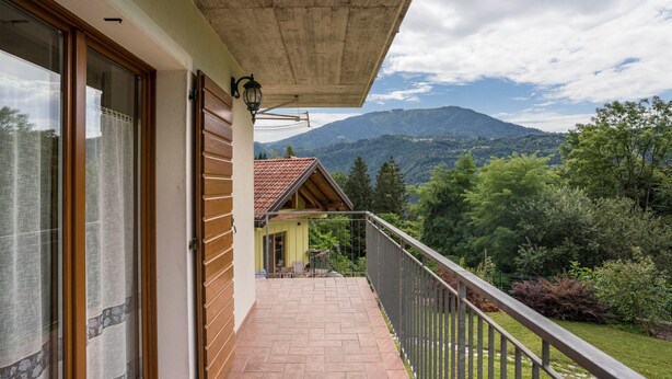 Een balkon met uitzicht op een berg, een houten deur en een raam met gordijnen.