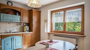 Een keuken met houten kastjes, een eettafel met placemats, een raam met uitzicht en een hangende lamp.