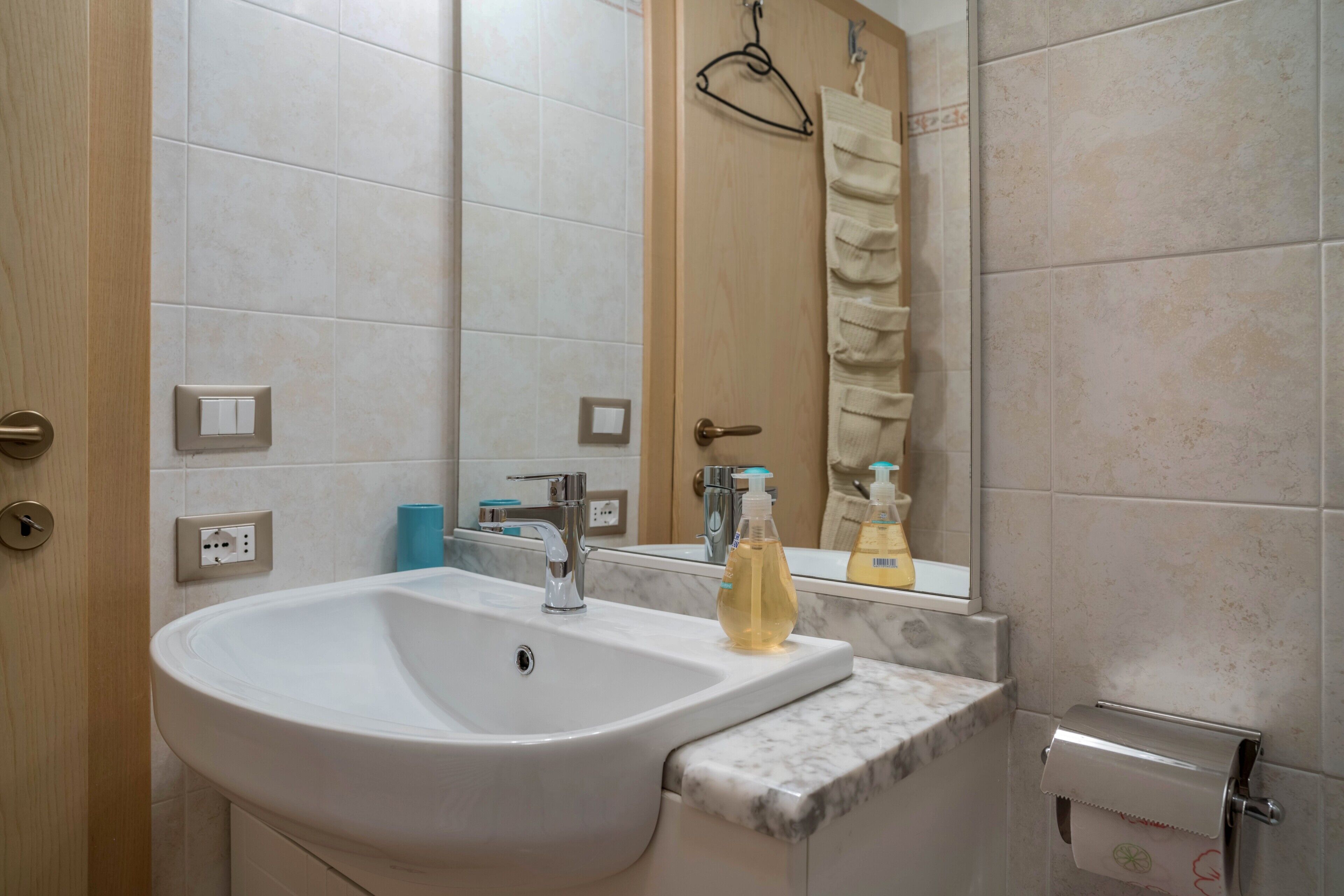 A bathroom with a white sink, mirror, towel rack, and toilet paper holder.