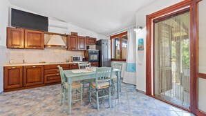 Une cuisine avec des meubles en bois, une table à manger avec des chaises et une porte-fenêtre coulissante donnant sur un balcon.