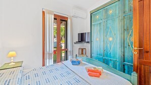 Une chambre à coucher comprenant un lit, une télévision, une armoire et une porte donnant sur un balcon.