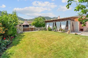 A well-maintained garden with a stone wall, a wooden pergola, and a stone chimney. - Villa "Vittoria" with Mountain View, 2 Private Terraces, and Wi-Fi (Villasimius)