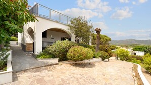 A modern building with an arched entrance, stone-paved courtyard, and surrounding greenery. - Holiday Home 'Villa Matteo' with Sea View, Wi-Fi and Air Conditioning (Perd'e Sali CA)