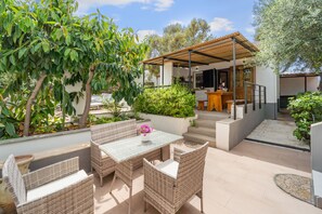 Un patio exterior con mobiliario de mimbre, una mesa con un florero y una zona cubierta con un banco.