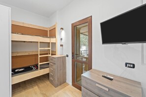 Ein Zimmer mit Etagenbetten, einem hölzernen Schminktisch, einem Fernseher und einer Tür zu einem Außenbereich.
