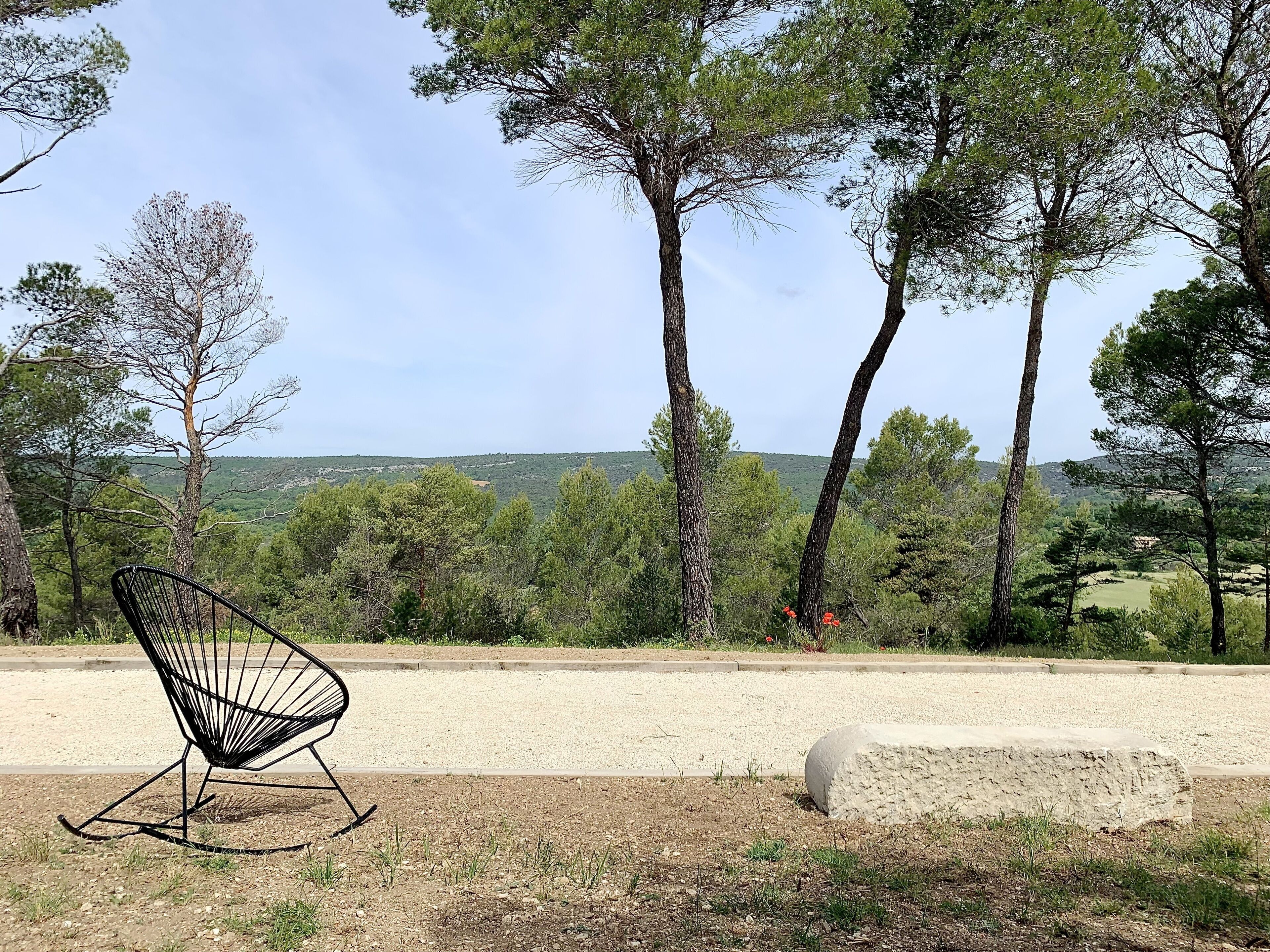 Une chaise placée dans un environnement naturel, au milieu des arbres, avec une vue sur un paysage lointain.