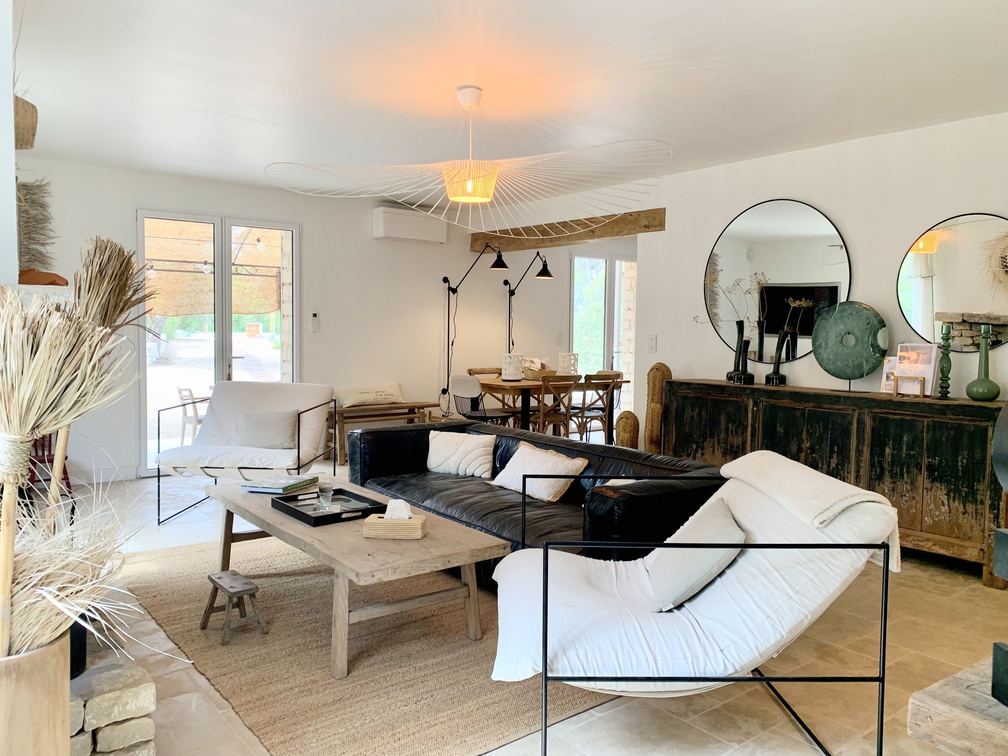Un salon moderne avec un canapé en cuir noir, des coussins blancs, une table basse en bois et un coin repas comprenant une table et des chaises en bois.