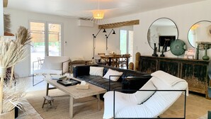A modern living room with a black leather sofa, white cushions, a wooden coffee table, and a dining area with a wooden table and chairs.