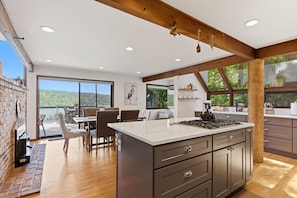A modern kitchen with a large island, wooden beams, and a view of the outdoors.