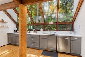 Una cocina moderna con un amplio ventanal, vigas de madera y lavavajillas.