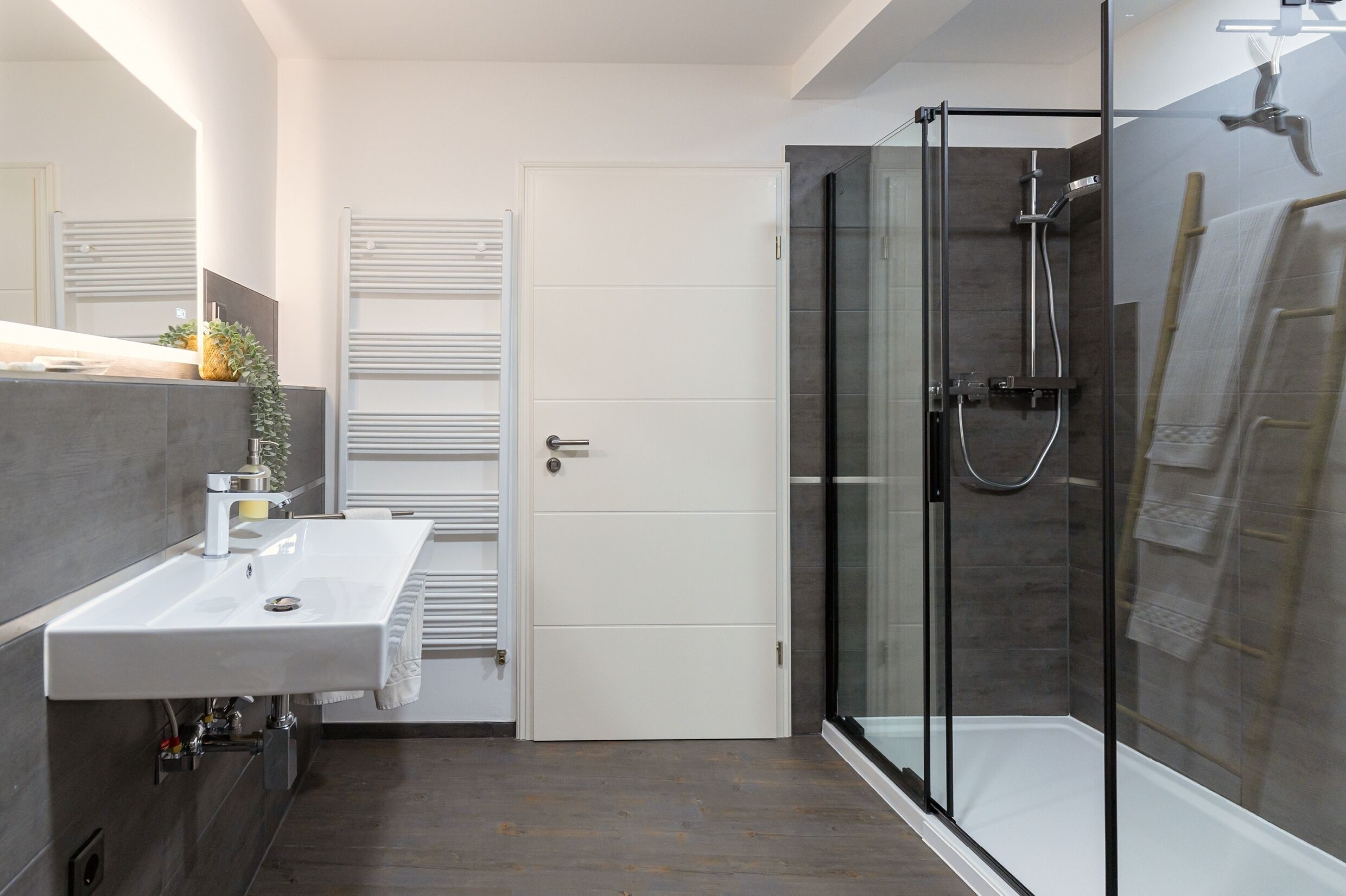 A modern bathroom with a glass-enclosed shower, a white sink, and a towel rack.