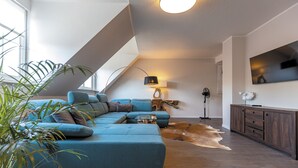 A modern living room with a sectional sofa, a flat-screen TV, and a ceiling fan. - Penthouse Hotel Garni am Domplatz (Erfurt)