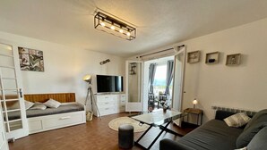 A compact, well-lit living room with a sofa, a bed, a TV, and a dining area with a table and chairs. - Port Apartment 2 Rooms Saint-Cyprien with Parking (Saint-Cyprien)